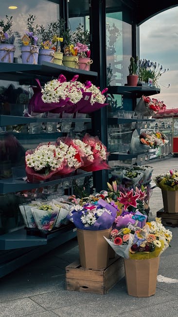 A display of various floral arrangements and bouquets at a flower shop, featuring a mix of fresh flowers in vibrant colors such as pink, white, purple, and yellow. The arrangements are wrapped in pape